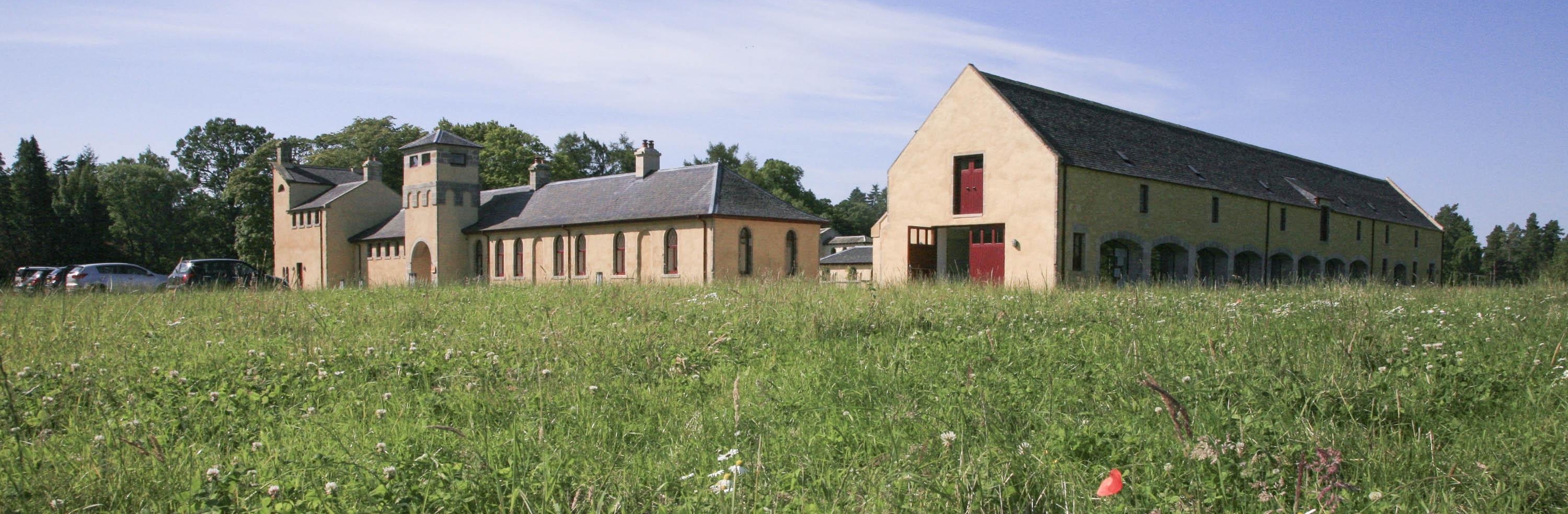 Renovated and converted agricultural buildings on the Altyre Estate, Moray. Used by Glasgow School of Art as a campus. View from across the field. Ochre rendered and washed stone buildings