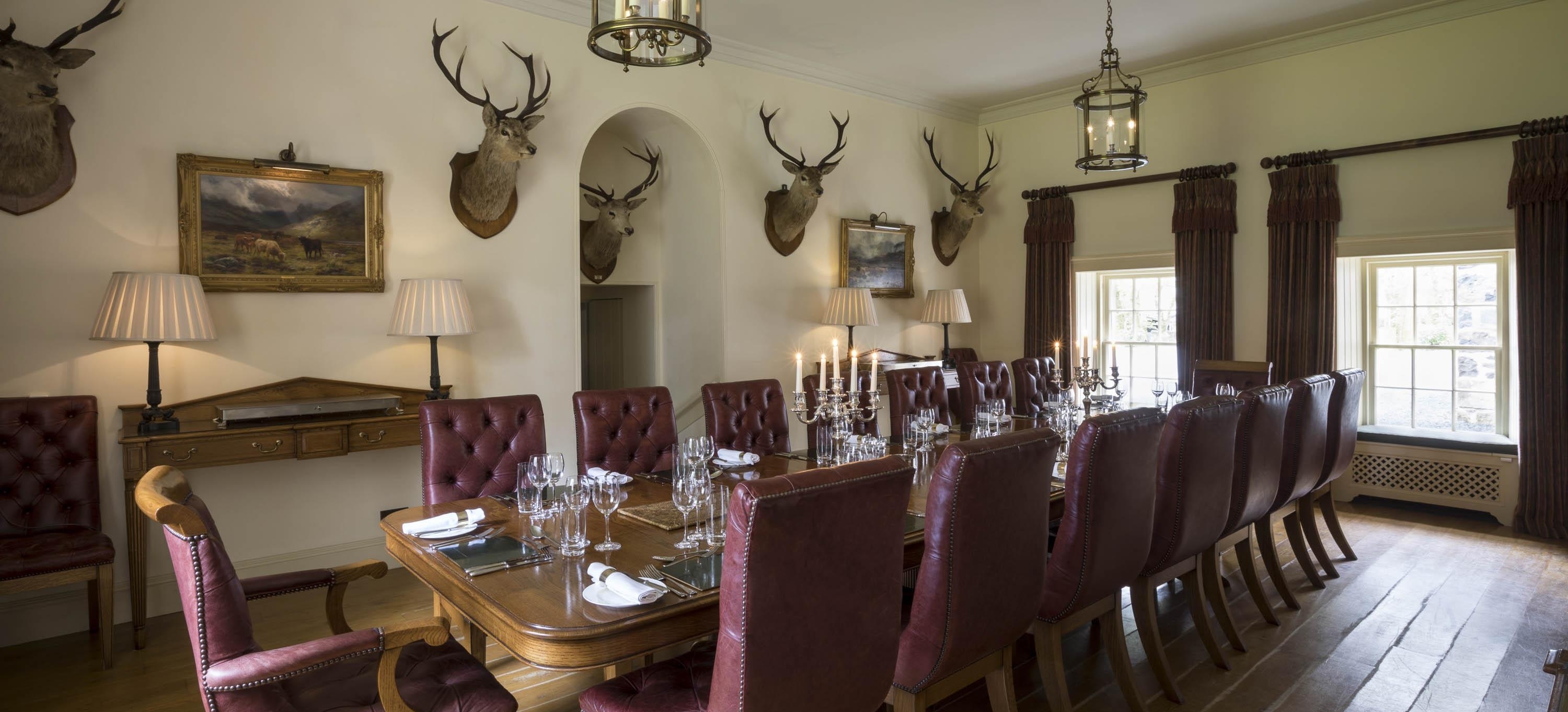 Traditional dining room in a Scottish country house. Stags heads, fireplace, large dining table with leather backed chairs.