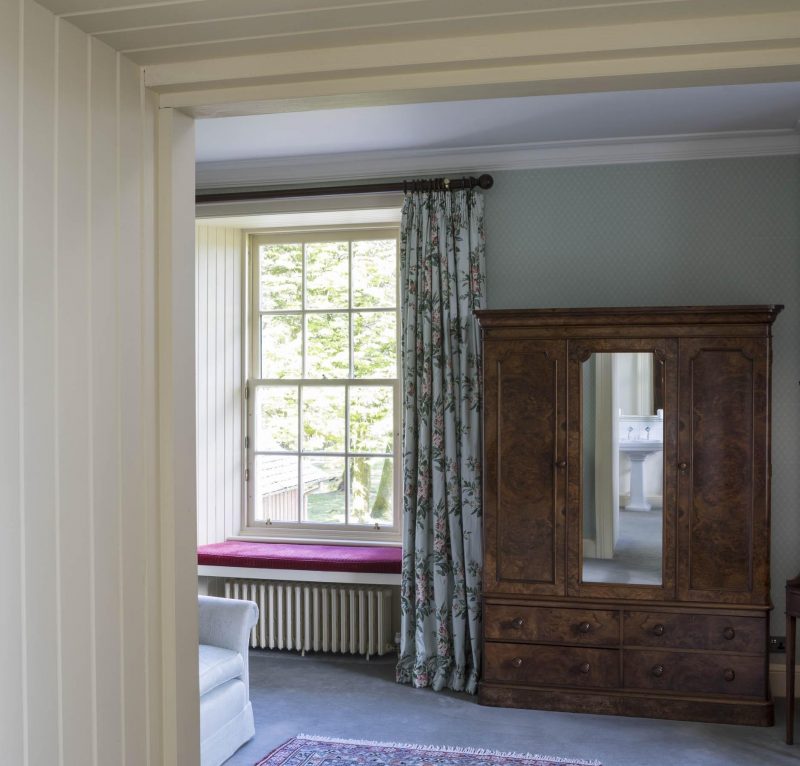 Refurbished bedroom in a Scottish country house. Antique Wardrobe and floral curtains. A leafy view through sash windows.