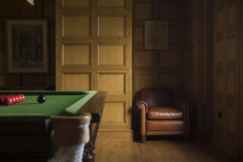 Oak panelled billiard room at a Scottish country house on the Isle of Mull. A leather armchair and edge of billiard table are shown.
