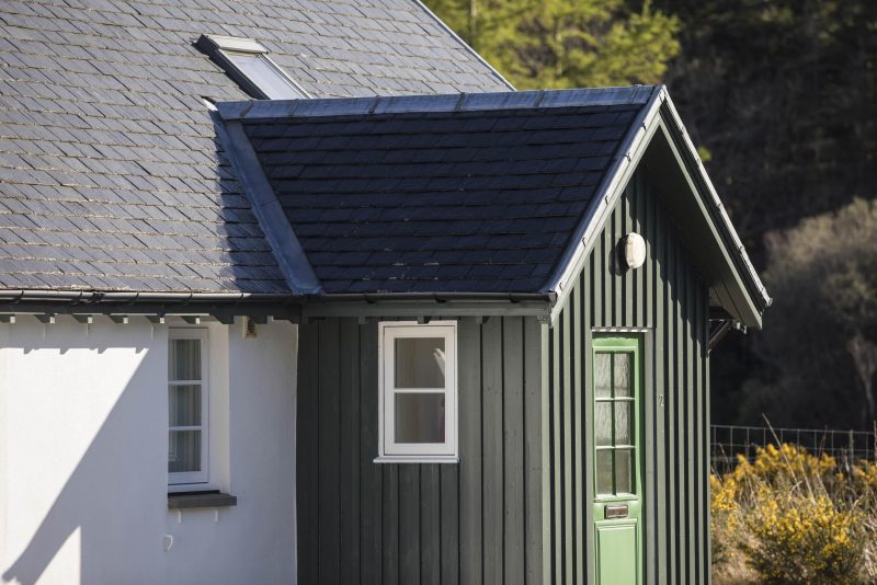 A timber porch on a white rendered and slate-roofed cottage. Timber is stained green.
