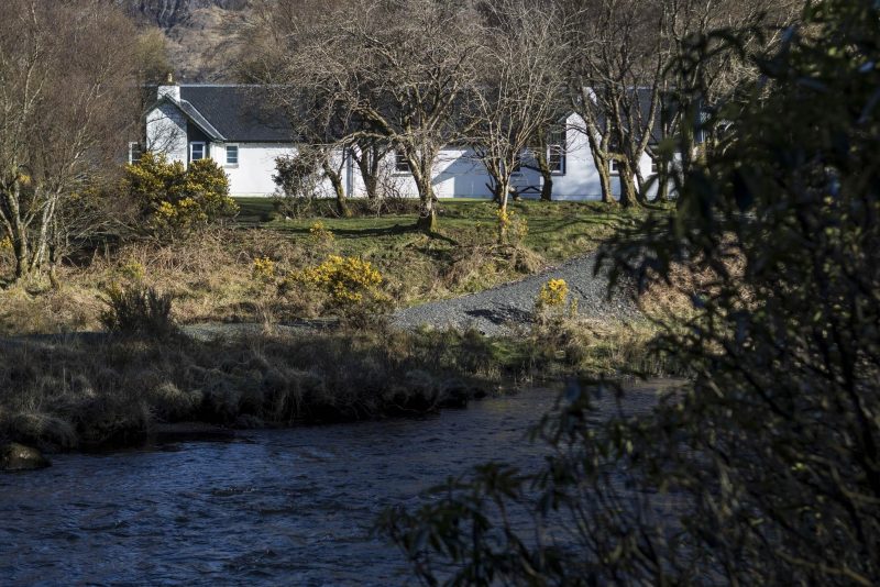View across a river to a pair of white rendered cottages.