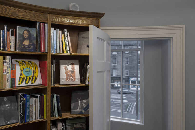 A view of a curved bookcase at Topping and Company, Edinburgh. Shelves filled with Art monographs. At the end of the shelf a curved door with a window behind, looking out onto the street.