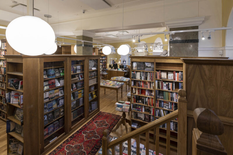 On the ground floor of the bookshop, tall shelves and tables are full of books.